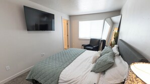 A bedroom with a bed, a chair, a TV, a window, and a mirror. - This 3BR/2BA retreat. North End Haven | Steps from Parks, Trails & Local Favorites Walking distance to Hyde Park  and Camel’s back park | Close to Boise White Water park and E Bikes For Rent it simple at this peaceful and centrally-located place. (Boise)