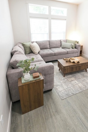 A living room with a grey sectional sofa, a wooden coffee table, a small side table with a plant, and a patterned rug. - This 3BR/2BA retreat. North End Haven | Steps from Parks, Trails & Local Favorites Walking distance to Hyde Park  and Camel’s back park | Close to Boise White Water park and E Bikes For Rent it simple at this peaceful and centrally-located place. (Boise)