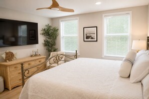 A bedroom with a bed, dresser, television, and windows.