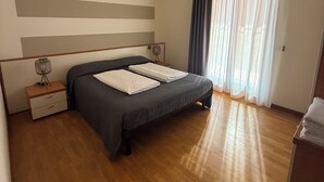 Quarto com cama, mesa de cabeceira, cômoda, janela com cortinas e luminária no teto.