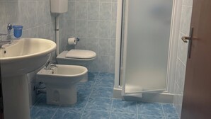 Um banheiro com pia, duas toaletes, chuveiro e porta-papel higiênico.
