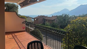 Uma varanda com vista para o mar e montanhas, chão de azulejos e grade de metal.