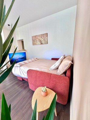Une chambre à coucher moderne avec un lit, une télévision, une plante et un tableau au mur.