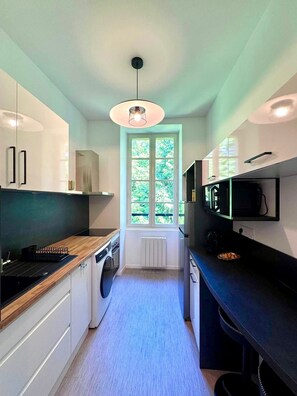 Une cuisine moderne dotée d’un îlot central, d’appareils électroménagers intégrés et d’une fenêtre laissant entrer la lumière naturelle.