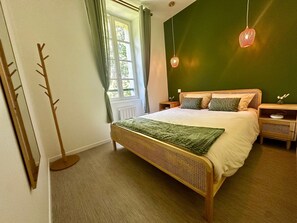 Ein Schlafzimmer mit Bett, Nachttischen, einem Fenster mit Vorhängen, einer Pendelleuchte und einem Kleiderhaken.