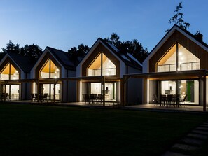 En rad moderna byggnader med träbeklädda tak och stora glasfönster, troligen en del av ett hotell eller ett semesterkomplex.