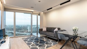 Ein modernes Wohnzimmer mit einem Glastisch, einem grauen Sofa und einem Esstisch mit Stühlen.