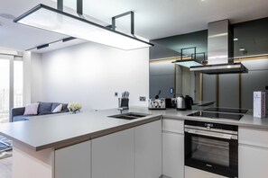 A modern kitchen with a central island, built-in oven, and a large window. - Stylish 2 Bed Flat in the Heart of Olympic Park (London)