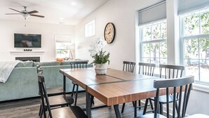 Un comedor con mesa de madera, sillas, un sofá, televisor, chimenea y un reloj en la pared.