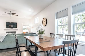 Un comedor con mesa de madera, sillas, un sofá, televisor, chimenea y un reloj en la pared.