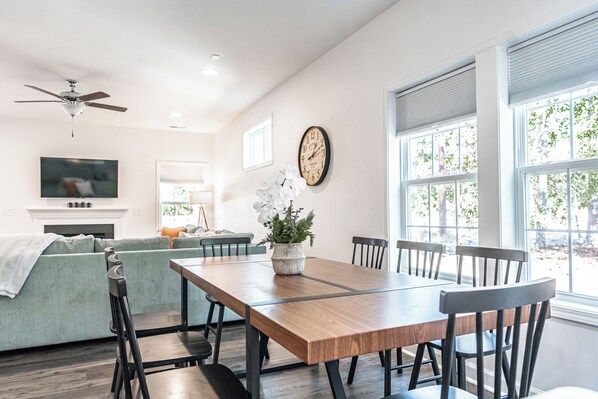 A dining area with a wooden table, chairs, a sofa, a TV, a fireplace, and a clock on the wall.
