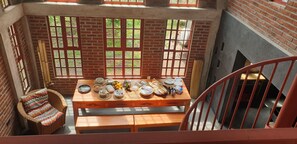 Un coin repas avec une table mise pour le repas, une chaise en osier et une vue par une fenêtre sur un mur de briques.