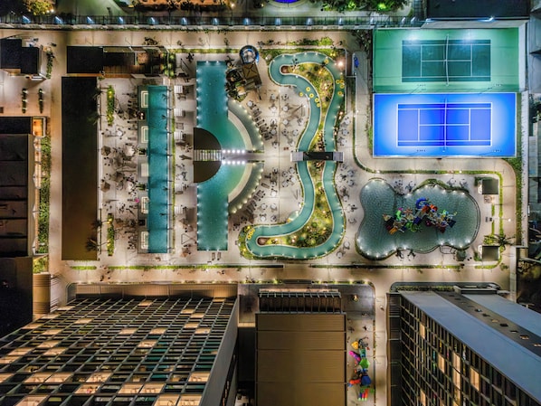 A rooftop pool area with a winding water feature, seating areas, and a tennis court. - Beach - GAV Hotéis e Resorts (Salinópolis)