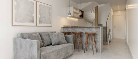Een moderne woonkamer met een grijze bank, houten krukjes en een keuken met een bar.