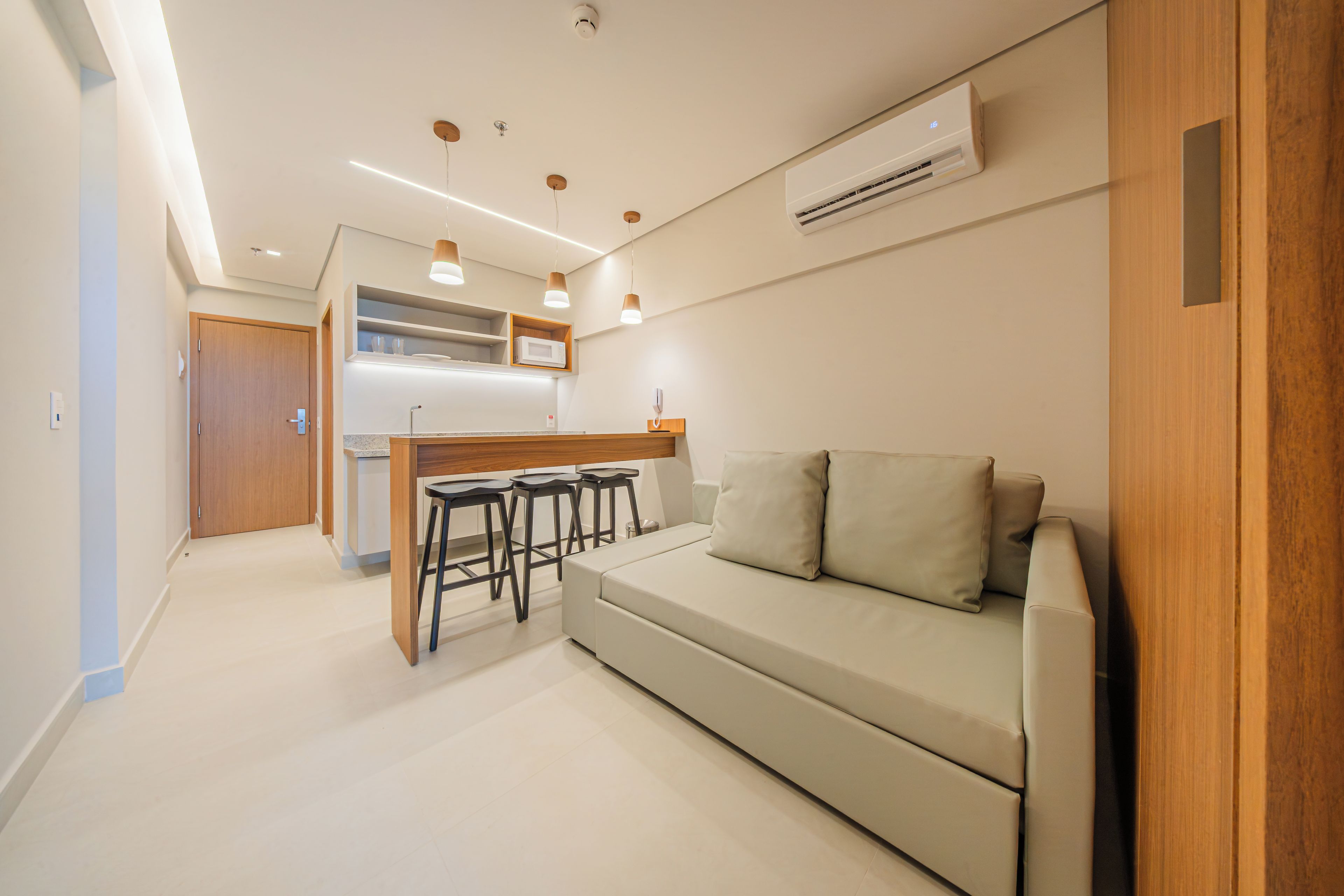 Una cocina moderna con microondas integrado, una barra de madera y una zona de estar con sofá y taburetes.