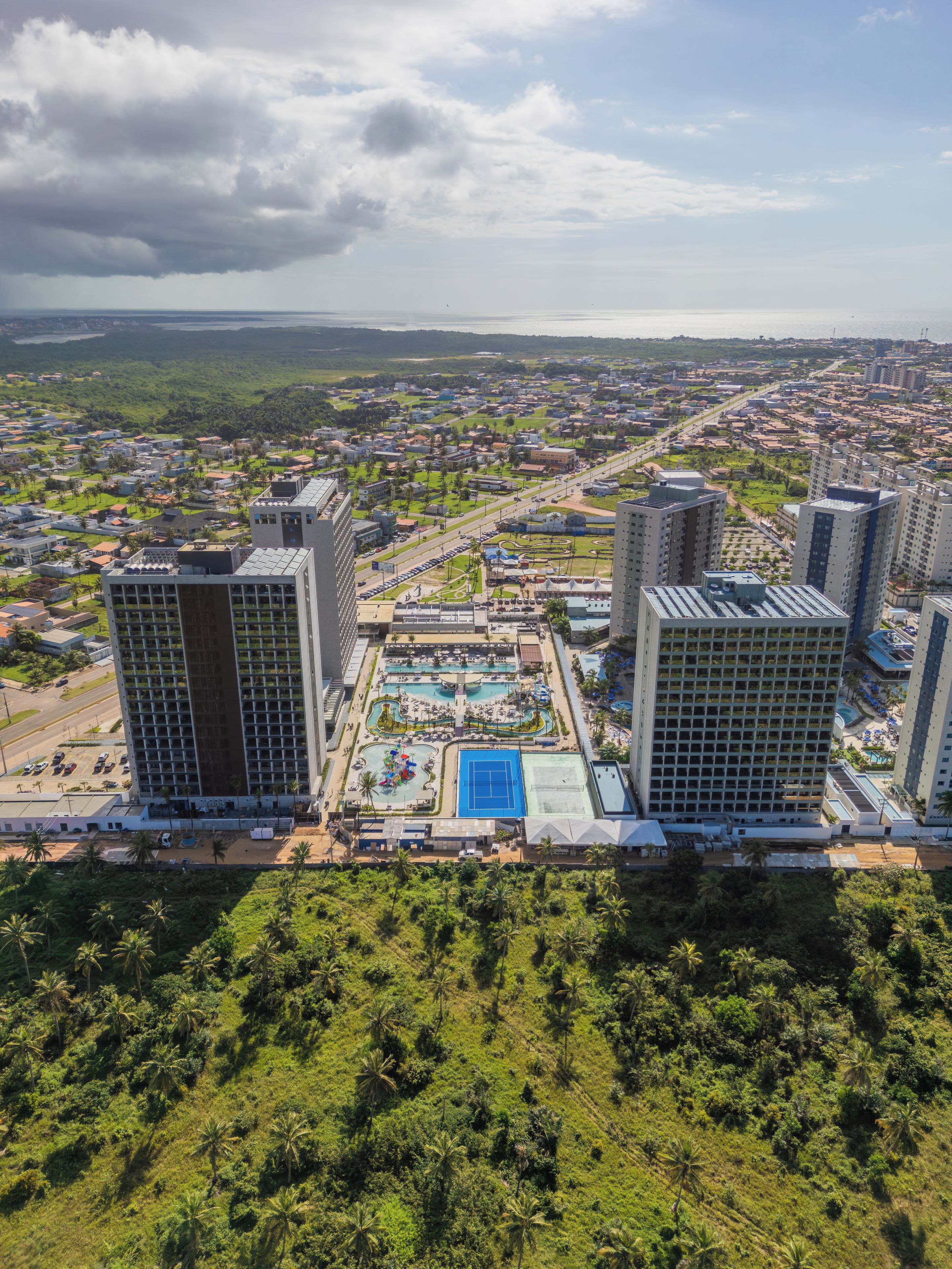 Hotel moderno com um pátio central que inclui uma piscina, cercado por vegetação exuberante e áreas residenciais.