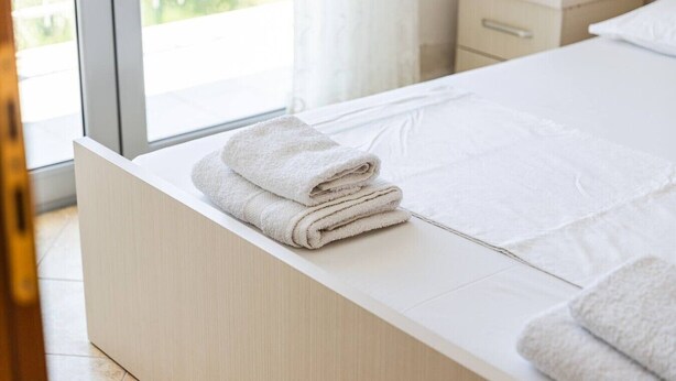 Una cama bien hecha con sábanas blancas y una toalla doblada al lado.