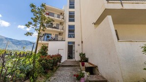 Un edificio de varios pisos con balcones, un acceso pavimentado y vistas a montañas.