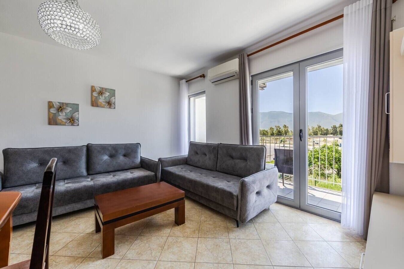 A modern living room with a grey sofa set, a wooden coffee table, and a chandelier.. Orikum Beachside Retreat | Apartment 2 by PikHost