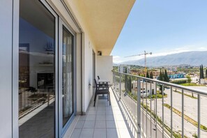 Un balcon avec une table et des chaises, une porte vitrée et une vue sur un chantier de construction et les montagnes.