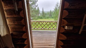 A wooden cabin with a balcony, a door leading to an outdoor area, and a view of a forest. - Serene 1-bedroom lakeside cabin at the arctic circle  perfect for a cozy getaway (Jokkmokk)