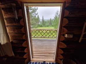 A wooden cabin with a balcony, a door leading to an outdoor area, and a view of a forest.