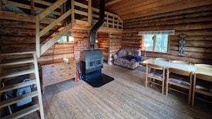 A log cabin interior with a wooden staircase, fireplace, sofa, and dining table. - Serene 1-bedroom lakeside cabin at the arctic circle  perfect for a cozy getaway (Jokkmokk)