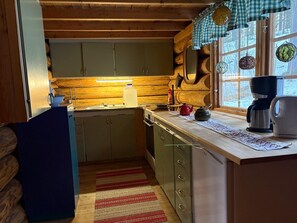 A compact kitchen with wooden cabinets, a countertop, a kettle, a coffee maker, and a window with a view of trees.