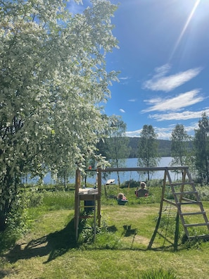 Et træsving, en stige og et græsplæne med et træ og en sø i baggrunden.