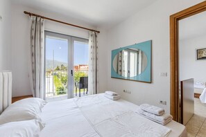 A hotel room with a bed, a balcony with a view, a large mirror, and a door leading to another room. - Orikum Beachside Retreat | Apartment 3 by PikHost (Orikum)
