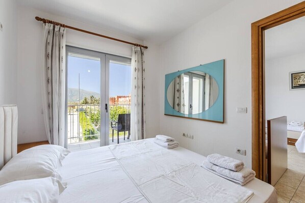 Une chambre d’hôtel avec un lit, un balcon offrant une vue, un grand miroir et une porte donnant sur une autre pièce.