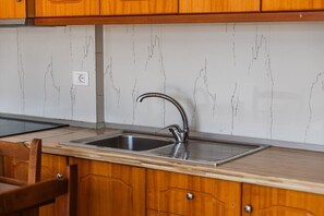 Eine Küche mit Holzausstattung, einem Edelstahl-Spülbecken und einer Marmor-Spritzschutzwand.
