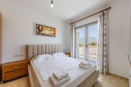 A bedroom with a bed, a nightstand, a painting, and a balcony with a view.. Orikum Beachside Retreat | Apartment 3 by PikHost