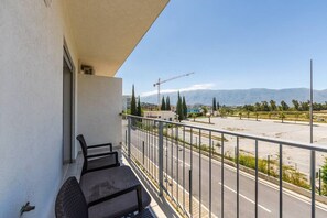 A balcony with two chairs, a view of a road with a construction crane, and distant mountains. - Orikum Beachside Retreat | Apartment 3 by PikHost (Orikum)