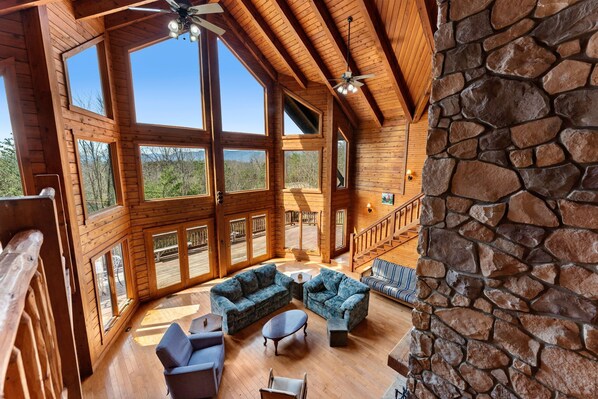 A spacious wooden interior with large windows, a stone wall, and a staircase.