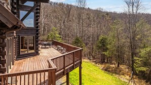 Una cabaña de troncos con terraza, mobiliario exterior y vistas a un paisaje boscoso.