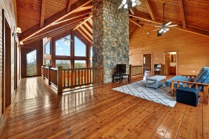 A spacious wooden interior with a stone pillar, a balcony, and a cozy seating area.