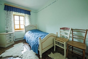 A bedroom with a bed, a chair, a dresser, and a window with curtains.