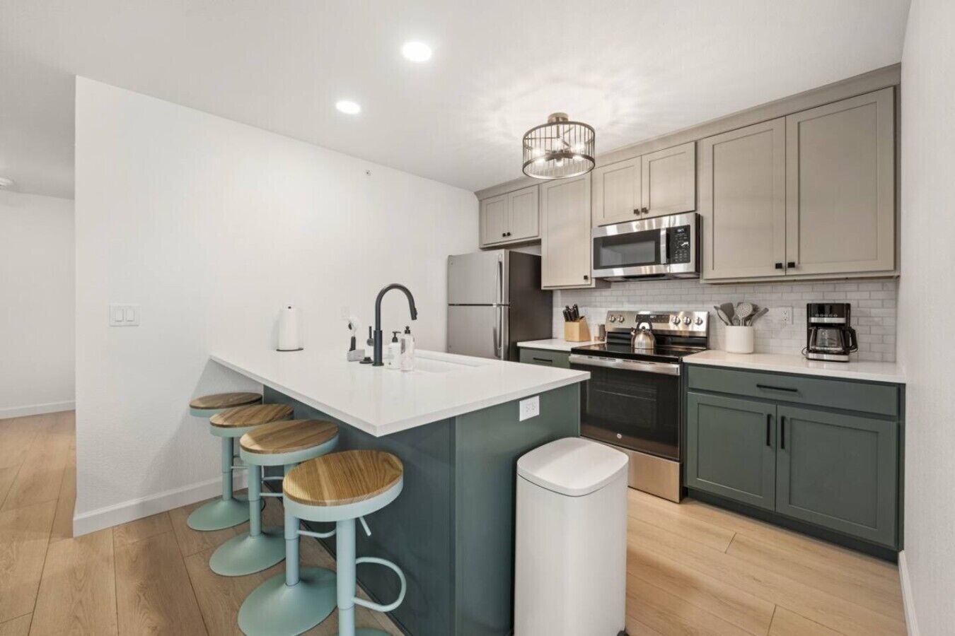 A modern kitchen with a central island, bar stools, stainless steel appliances, and light-colored cabinetry.
