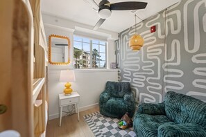 Una habitación con una pared estampada, un ventilador de techo, una ventana, una lámpara, una silla, un sofá y una alfombra.