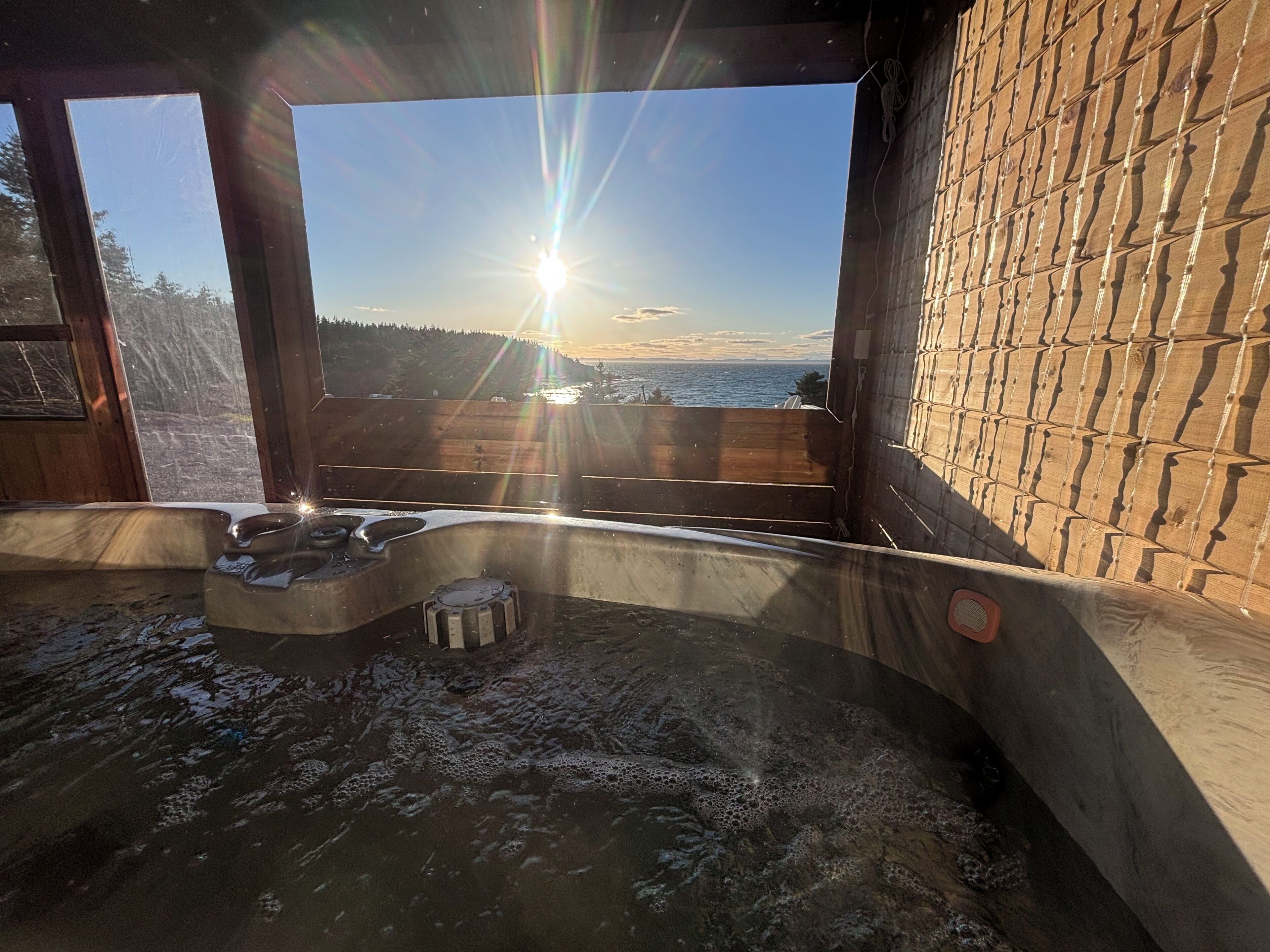 A hot tub with a view of the sunset over the ocean, wooden walls, and a clear sky.. Oceanfront Boutique Retreat~Hot Tub~Woodstove