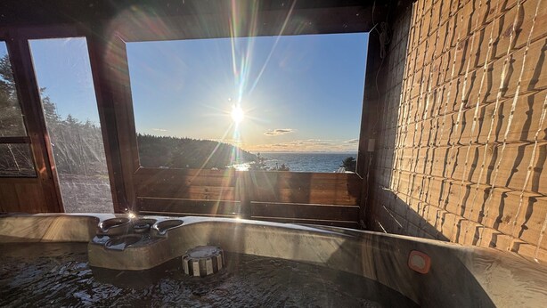 A hot tub with a view of the sunset over the ocean, wooden walls, and a clear sky. - Oceanfront Boutique Retreat~Hot Tub~Woodstove (Hearts Delight-Islington)