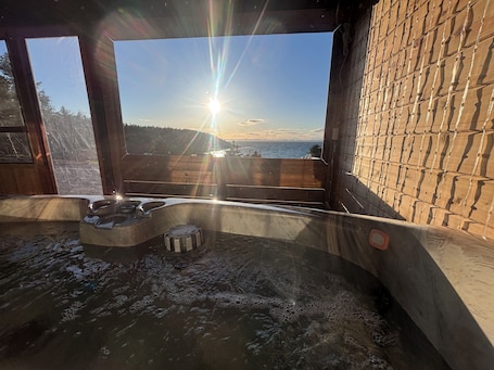A hot tub with a view of the sunset over the ocean, wooden walls, and a clear sky.. Oceanfront Boutique Retreat~Hot Tub~Woodstove