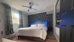 A bedroom with a bed, a ceiling fan, a patterned wall, and a door. - Oceanfront Boutique Retreat~Hot Tub~Woodstove (Hearts Delight-Islington)