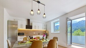 Una cocina moderna con comedor, un ventanal con vistas a la montaña y lámparas colgantes.