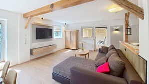 Una sala de estar moderna con un televisor grande, vigas de madera, un sofá y una zona de comedor.