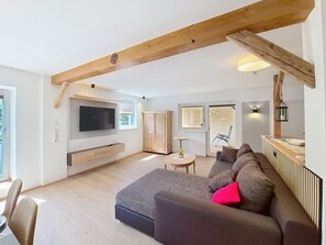 Ein modernes Wohnzimmer mit großem Fernseher, Holzbalken, einer Couch und einem Essbereich.
