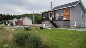 A two-story building with a porch, a staircase, and a picnic table in the yard. - Oceanfront Boutique Retreat~Hot Tub~Woodstove (Hearts Delight-Islington)