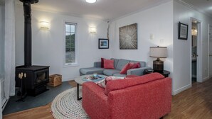 A living room with a fireplace, a sofa, a coffee table, and a lamp. - Oceanfront Boutique Retreat~Hot Tub~Woodstove (Hearts Delight-Islington)