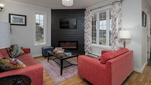 A living room with a fireplace, red sofas, a TV, and a chandelier.